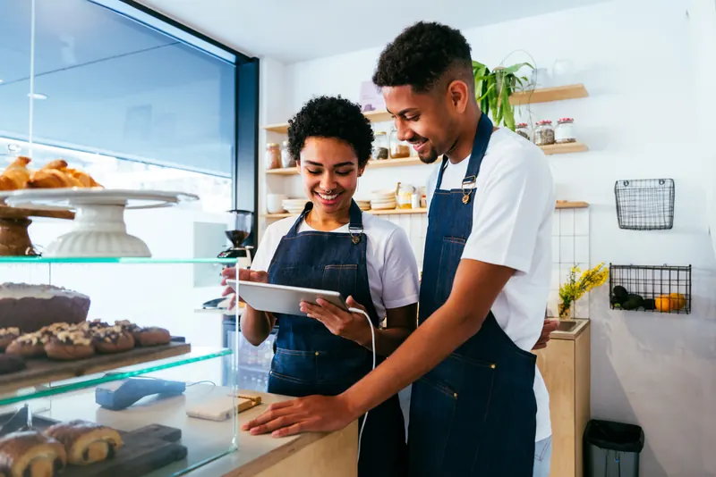 Zwei Mitarbeitende einer Bäckerei schauen an der Theke gemeinsam auf ein Tablet